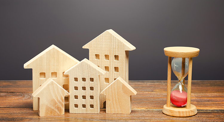 Wooden figures of houses and sand hourglass. Mortgage and loan concept. Temporary rental housing and residence permit. Time to pay taxes and bills. Realtor services for a quick search for options.