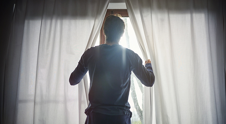 Man opening curtains in bedroom