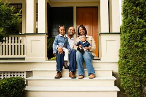 Portrait of a young family sitting on the steps in front of their house.