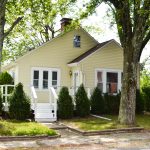 Front of a yellow cape code house with white deck.