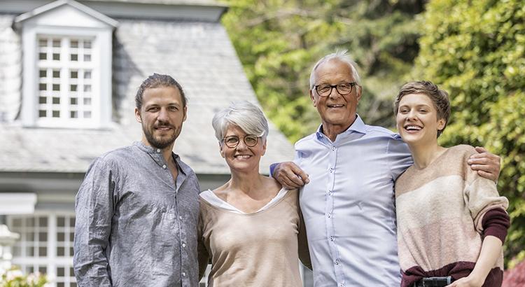Happy senior couple with adult children standing in garden of their home